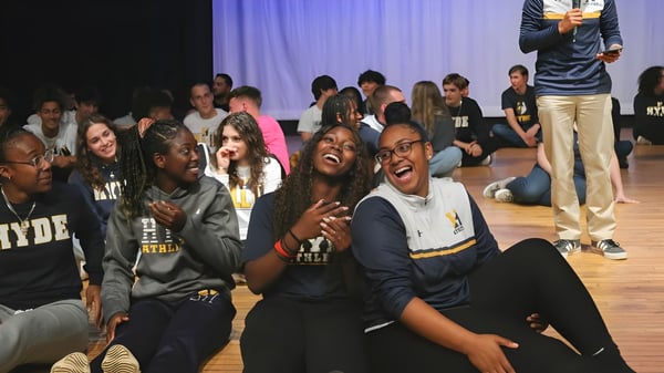 Un grupo de estudiantes de la Hyde School está sentado y de pie en una sala débilmente iluminada conversando.