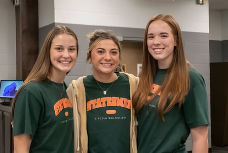 Tres estudiantes sonrientes están juntas en un pasillo del campus de Illinois Eastern Community Colleges.