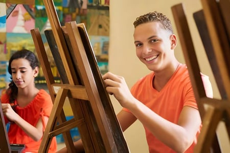 Dos estudiantes de la Imagine High Integrated Arts and Technology Secondary School pintan en la clase de arte sobre lienzos.