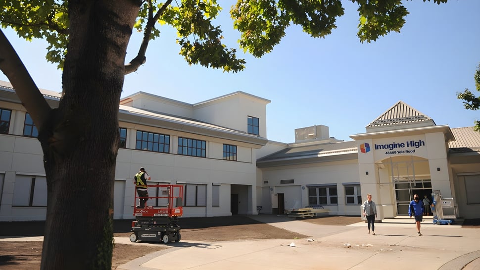 Un moderno edificio escolar de la Imagine High Integrated Arts and Technology Secondary School con un elevador para trabajos de construcción en primer plano.