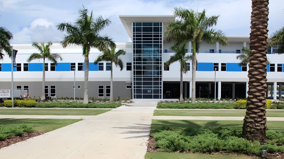 El moderno edificio de varios pisos de la IMG Academy con grandes ventanas y palmeras en primer plano bajo un cielo azul.