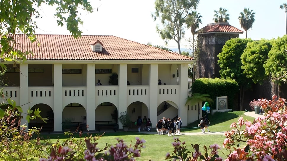 El edificio de la Immaculate Heart High School con un tejado de tejas y arcos está rodeado de un verde cuidado y flores en flor.