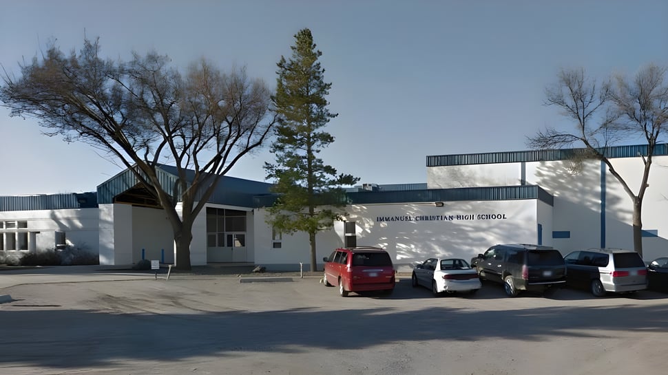 El edificio de la Immanuel Christian Secondary School se encuentra detrás de árboles y coches estacionados.