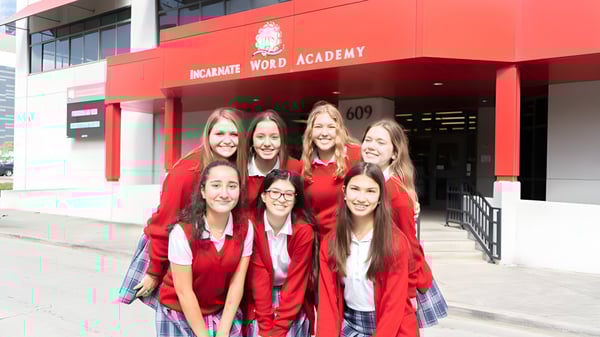 Un grupo de jóvenes mujeres está de pie en vestidos de graduación rojos frente al edificio de la Incarnate Word Academy.
