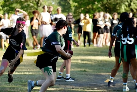 Un grupo de estudiantes de la Indian River Charter High School se reúne en un campo deportivo con árboles alrededor.