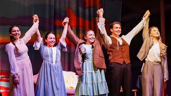 Cinco mujeres están en el escenario de la Indian River Charter High School levantando los brazos en un gesto festivo.