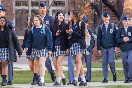 Estudiantes de la Indiana Private Highschool caminan juntos por el campus con edificios de ladrillo en el fondo.
