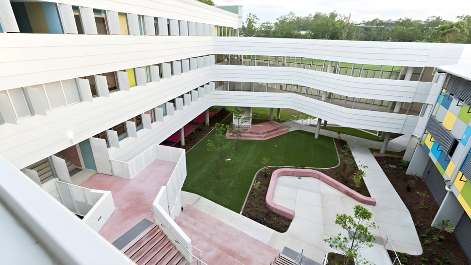Se puede ver el moderno edificio de varios pisos de la Indooroopilly State High School con un patio y caminos rosas.