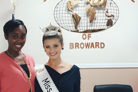Dos mujeres posan frente a un fondo con el letrero de la International School of Broward.