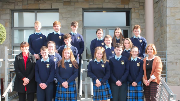 Un grupo de estudiantes en uniformes escolares está de pie frente a un edificio de piedra con grandes ventanas en el campus del Inver College.