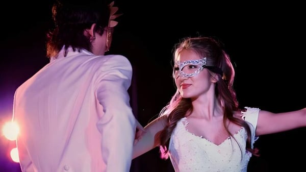 Una mujer lleva un vestido blanco y una máscara en un evento de la Iolani School con colorida iluminación de fondo.