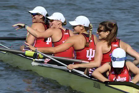 Estudiantes de la Ipswich State High School están sentadas en uniformes rojos con gorras blancas en un pequeño bote sobre el agua.