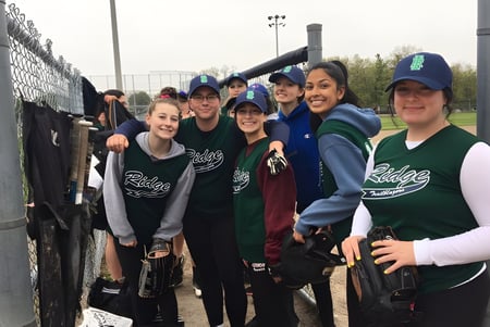 Un grupo de estudiantes de la Iroquois Ridge High School posan juntos frente a un campo deportivo cercado.