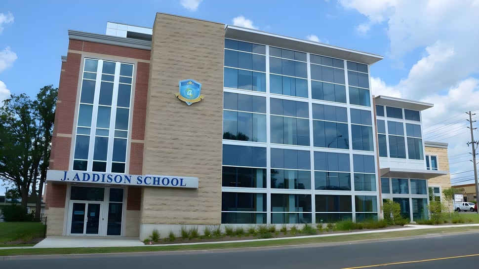 El moderno edificio escolar de la J. Addison School con grandes ventanales de vidrio se encuentra en un entorno similar a un parque.