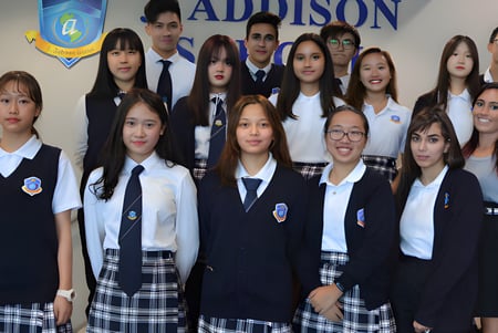 Un grupo de estudiantes de la J. Addison School posa frente a un fondo con el nombre y el logo de la escuela.