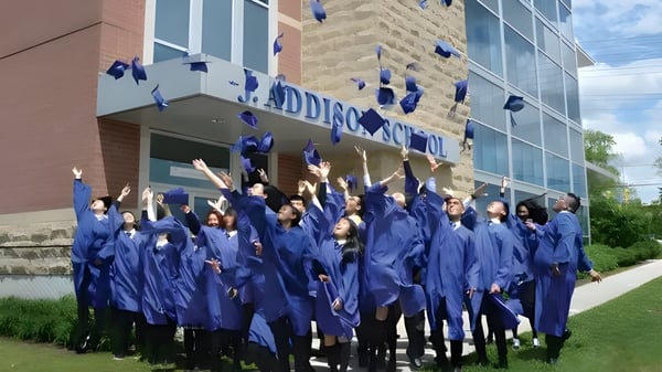 Un grupo de graduados de la J. Addison School celebra frente a un edificio de ladrillo sus logros académicos.