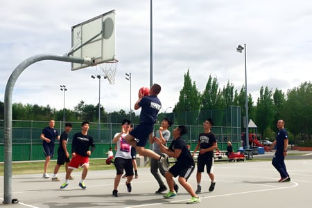 Estudiantes de la J.N. Burnett Secondary School juegan baloncesto en un patio al aire libre bajo un cielo nublado.