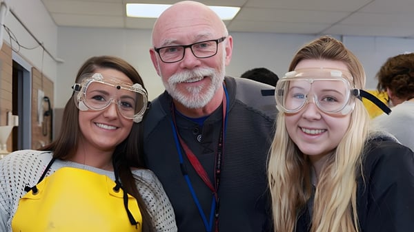 Tres personas con gafas de protección están en un interior en el campus de la James Fowler High School.