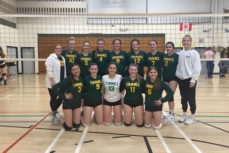 Un grupo de jugadoras de voleibol en camisetas verdes posan en el campo de voleibol de la James M. Hill Memorial High School.