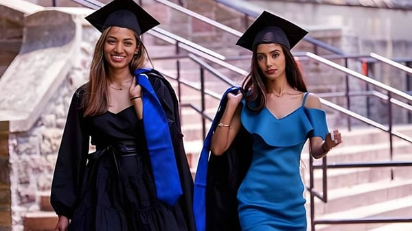 Dos estudiantes en ropa de graduación posan en una escalera frente a un edificio de ladrillo en el campus del Jarvis Collegiate Institute.
