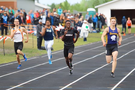 Estudiantes de Jasper Place High School corren en competencia en la pista con espectadores y edificios escolares en el fondo.