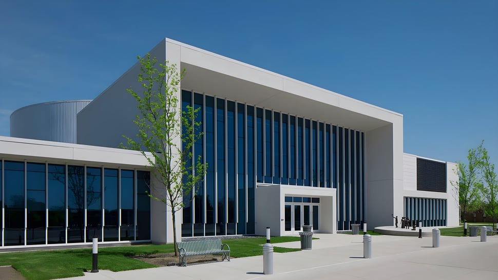 El moderno edificio de la Jenison High School con fachada de vidrio está integrado en un paisaje verde bajo un cielo despejado.