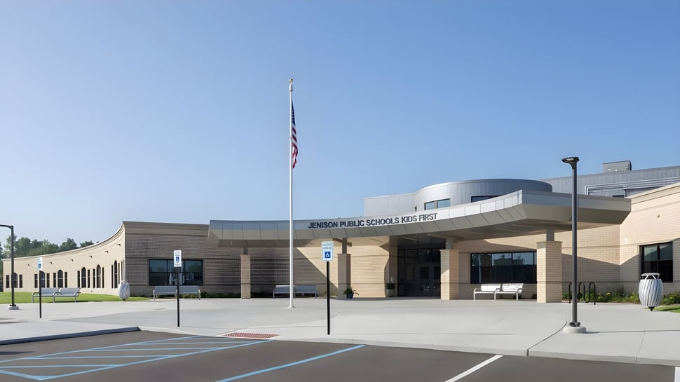 El moderno edificio con techo curvado y bandera americana frente a la Jenison Public Schools.