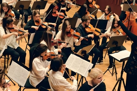 Una gran orquesta se presenta en el escenario de la Jesus and Mary Secondary School vestida de manera formal y toca varios instrumentos de cuerda.