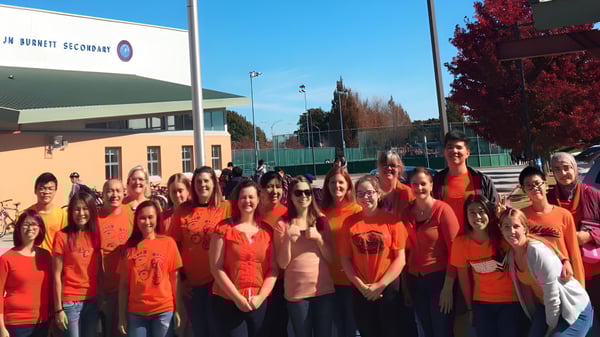 Un grupo de estudiantes de la J.N. Burnett Secondary School está frente a un edificio con camisetas rojas.