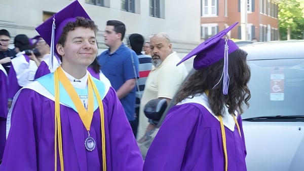 Estudiantes de la John Bapst Memorial High School llevan togas y birretes morados en una ceremonia de graduación al aire libre.