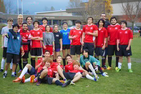 Un grupo de estudiantes de la John Barsby Secondary School está de pie en camisetas rojas en un campo de deporte frente a un edificio escolar.