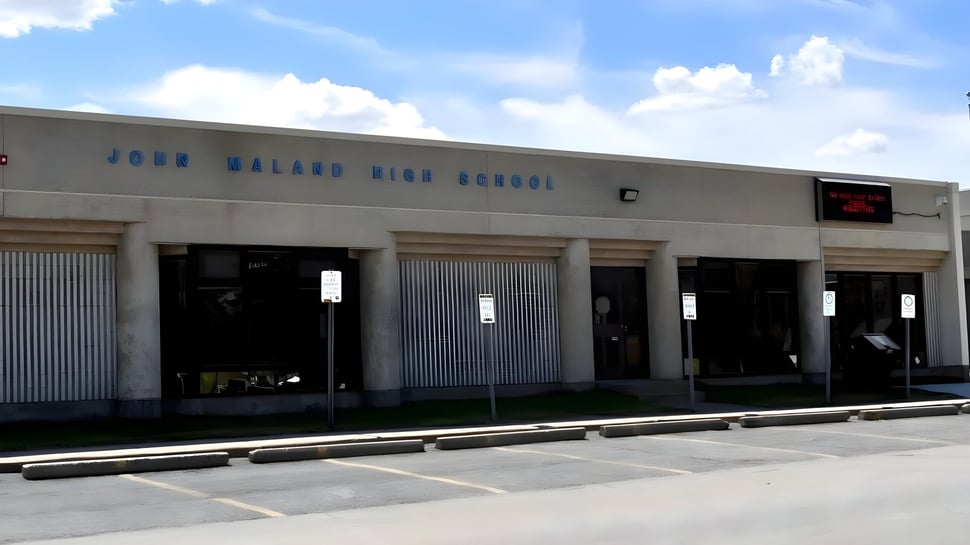 El gran edificio escolar gris de la John Mallard High School es claramente visible con su nombre en la fachada.