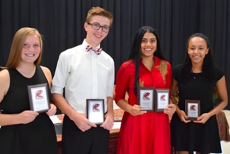 Cuatro personas sostienen premios en la mano durante una entrega de premios en la John McGregor Secondary School.