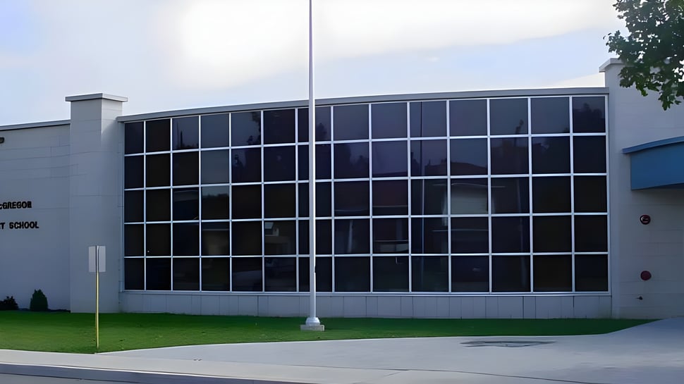 El moderno edificio de varios pisos de la John McGregor Secondary School se encuentra en un área verde con árboles.