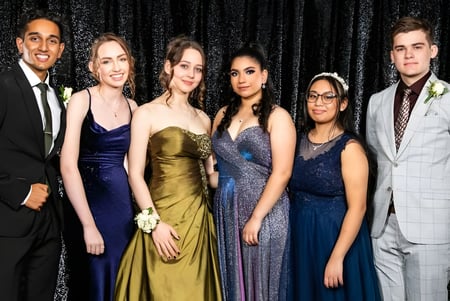 Seis personas posan frente a un fondo negro en el campus del John Paul College.