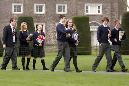 Un grupo de estudiantes de la John Scottus Secondary School está de pie sobre el césped frente a un edificio de ladrillo.