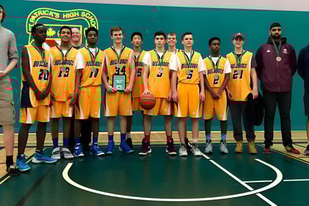 Un grupo de estudiantes de la John McCrae Secondary School está junto en la cancha de baloncesto con camisetas amarillas.
