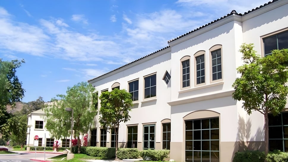 El edificio de varios pisos con ventanas de arco y techo de tejas en el campus de la JSerra Catholic High School está rodeado de vegetación verde.
