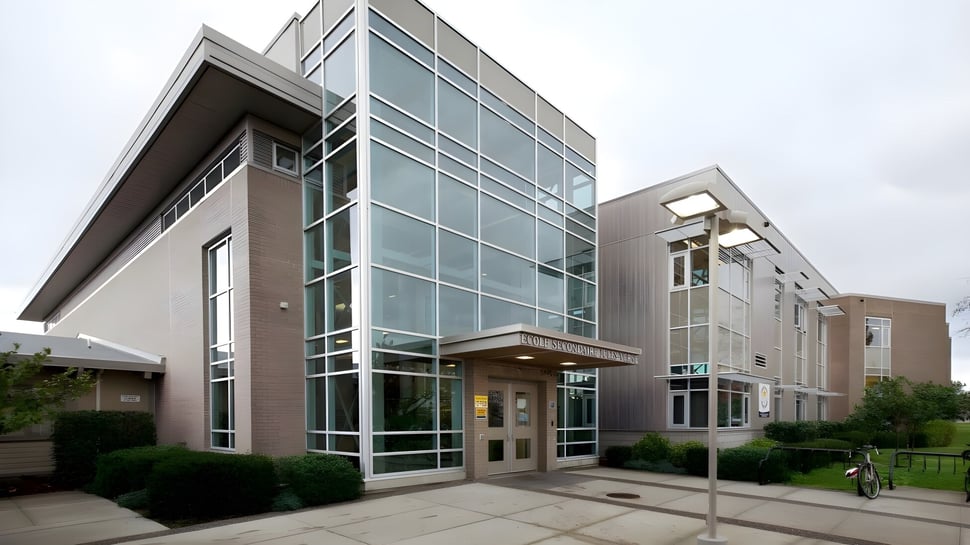 El moderno edificio de varios pisos con fachada de vidrio de la Jules Verne School Vancouver está rodeado de un camino pavimentado y áreas verdes.
