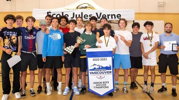 Un grupo de estudiantes de la Jules Verne school Vancouver posan en el gimnasio con una pancarta escolar y una tabla de campeonatos.