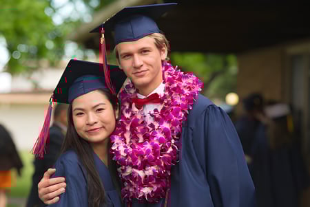 Dos graduados con birretes y togas están juntos en el campus de la Justin Siena High School.