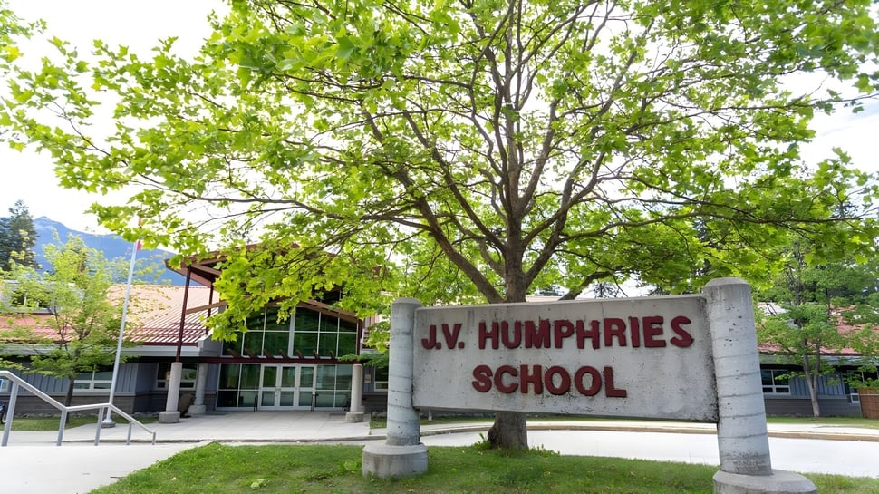 Un gran árbol con densa hoja verde está en la entrada del edificio escolar de la J.V. Humphries Secondary School.