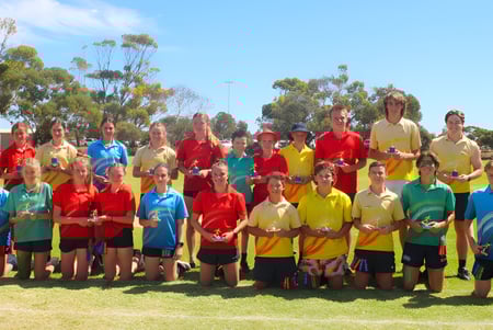 Un grupo de estudiantes de la Kadina Memorial School está en el campo deportivo sobre un césped frente a árboles bajo un cielo despejado.