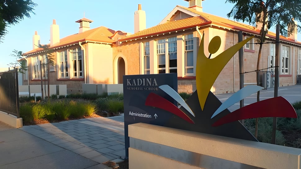 El colorido y decorado edificio de la Kadina Memorial School está rodeado de palmeras y se encuentra junto a un camino pavimentado.