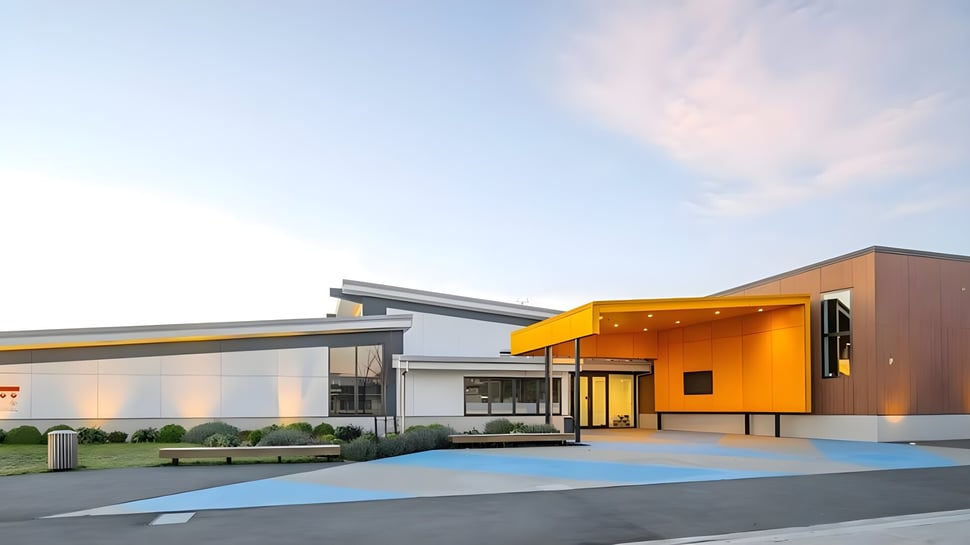El moderno y colorido edificio de la Kaiapoi High School se encuentra frente a un cielo despejado y está rodeado de caminos y vegetación.