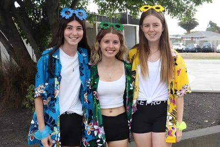 Tres estudiantes de la Kaiapoi High School posan riendo al aire libre frente a árboles y edificios.