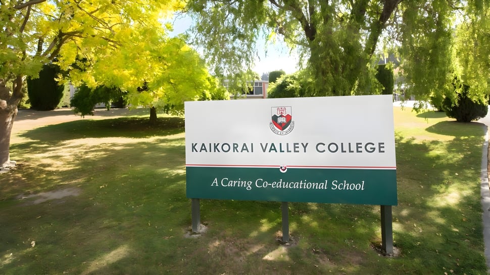 El cartel del Kaikorai Valley College está rodeado de árboles con hojas amarillas en un entorno similar a un parque.