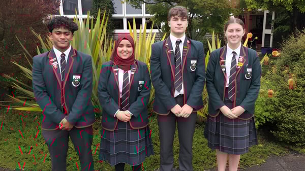 Un grupo de estudiantes del Kaikorai Valley College está frente a un edificio con mucho verde al fondo.