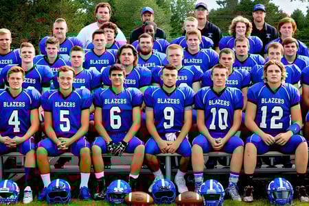 Un grupo de jóvenes jugadores de fútbol de la Kalkaska High School está sentado juntos al aire libre en un área de césped.