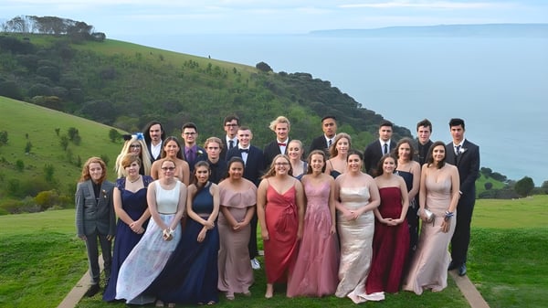 Un grupo de personas en ropa formal se encuentra en un camino frente a colinas verdes en el terreno de la Kangaroo Island Community Education.